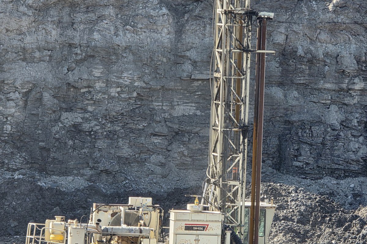 A blast-hole drill working against a rock highwall at a quarry.