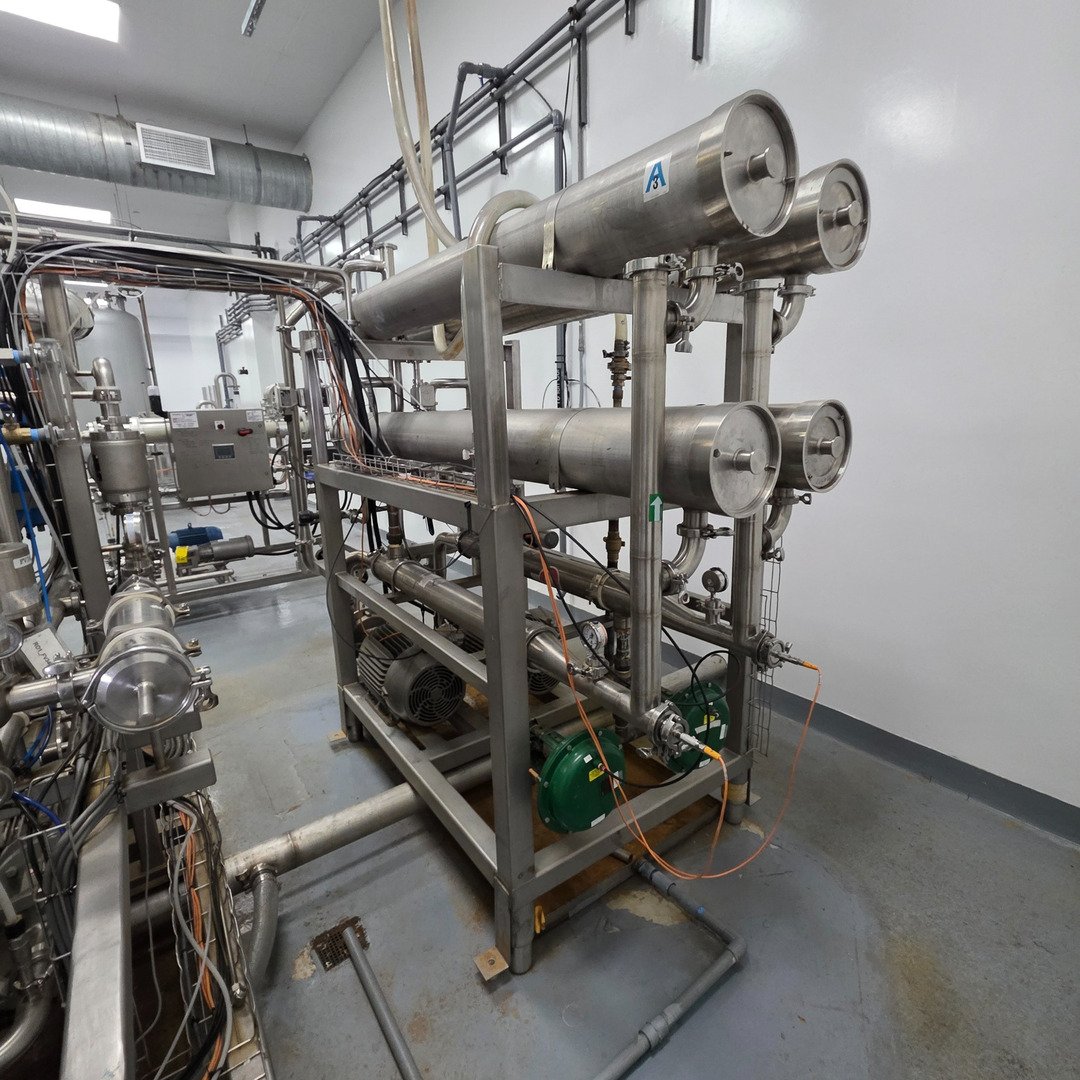 A stainless shell-and-tube heat-exchanger skid with process piping and pumps in a chemical plant.