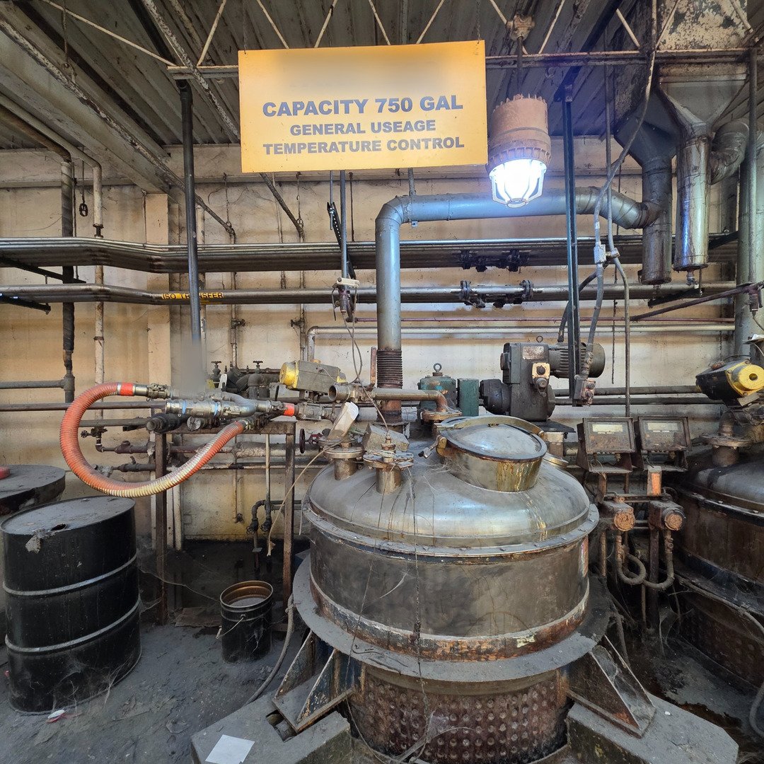 A jacketed 750-gallon reactor with agitator drive, nozzles, and process piping in a chemical manufacturing plant.
