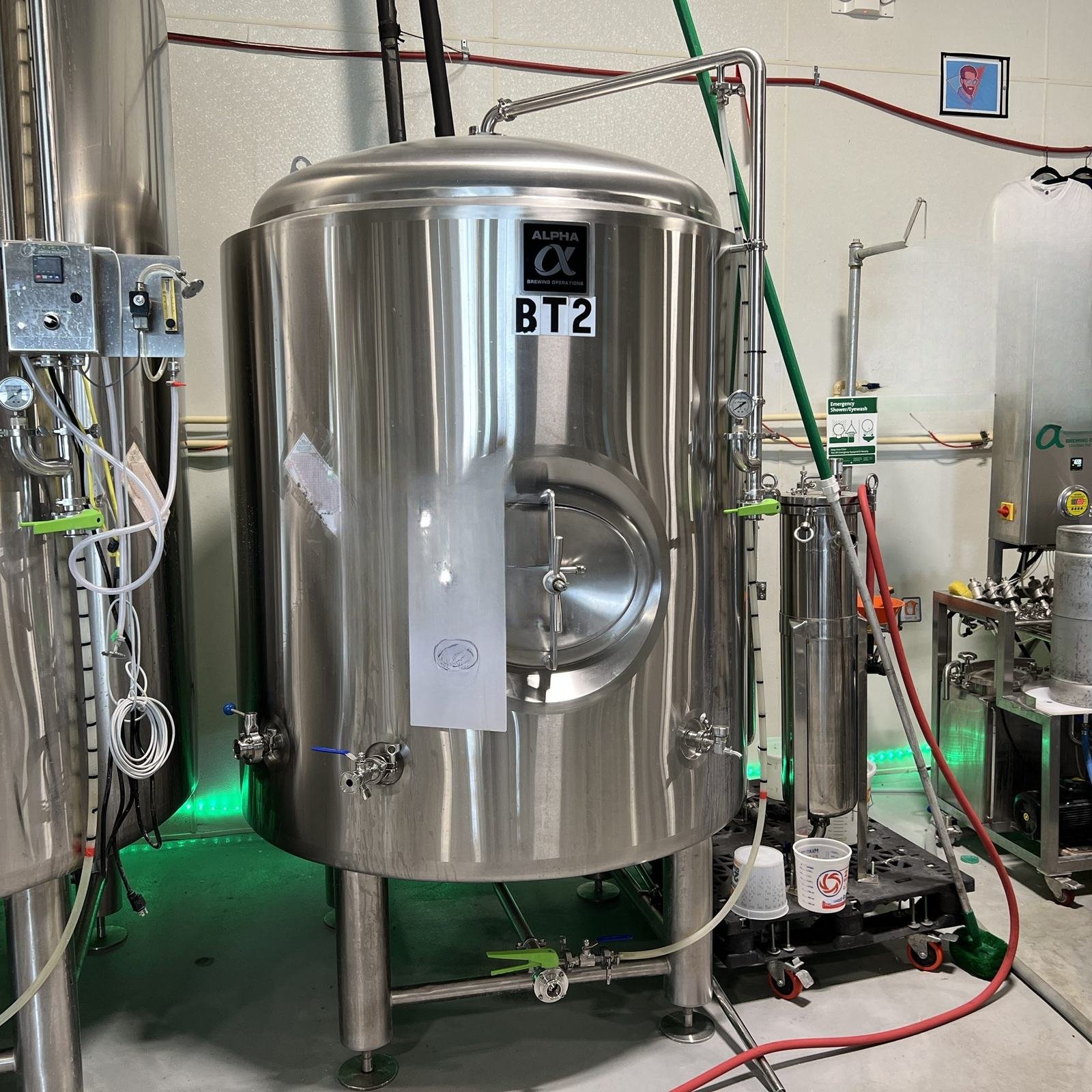 A jacketed stainless storage tank with valves and fittings in a beverage cellar.