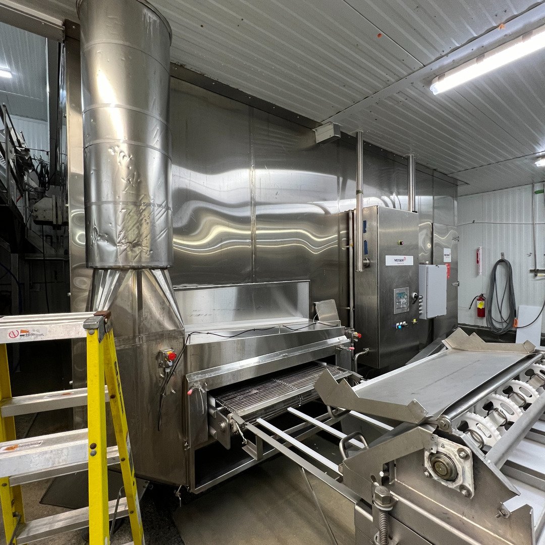 A cryogenic tunnel freezer with a stainless exhaust stack and control panel in a poultry processing plant.