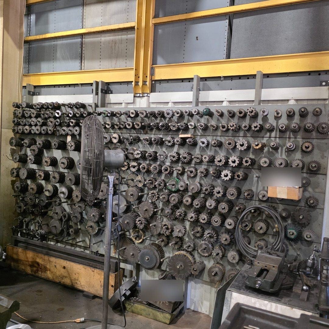 A wall rack holding dozens of CNC tool holders and cutting heads beside the machines.