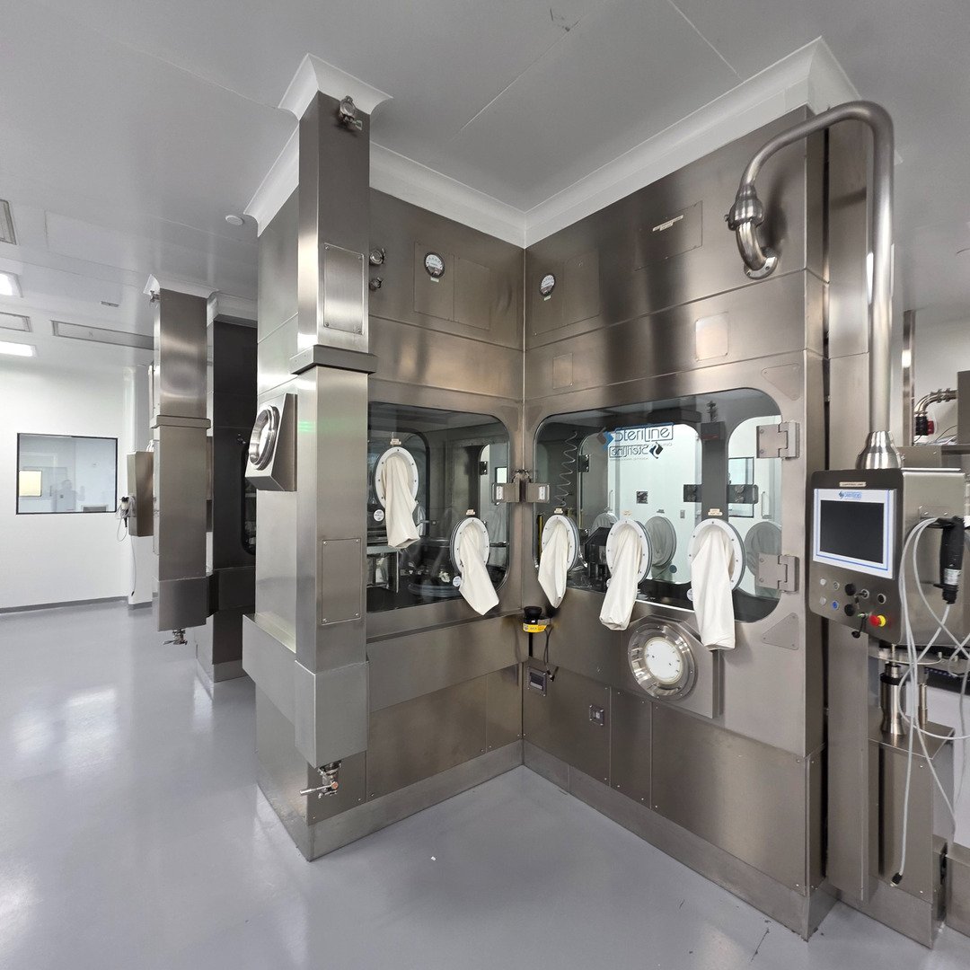 A stainless barrier isolator with glove ports, viewing windows, and a control panel on an aseptic line in a pharmaceutical cleanroom.