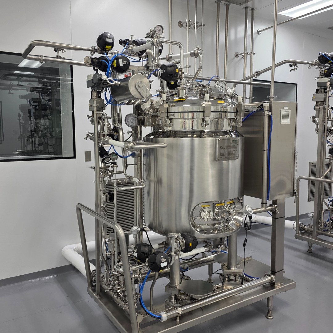 A skid-mounted, jacketed stainless process vessel with sanitary piping and an HMI control panel in a pharmaceutical cleanroom.