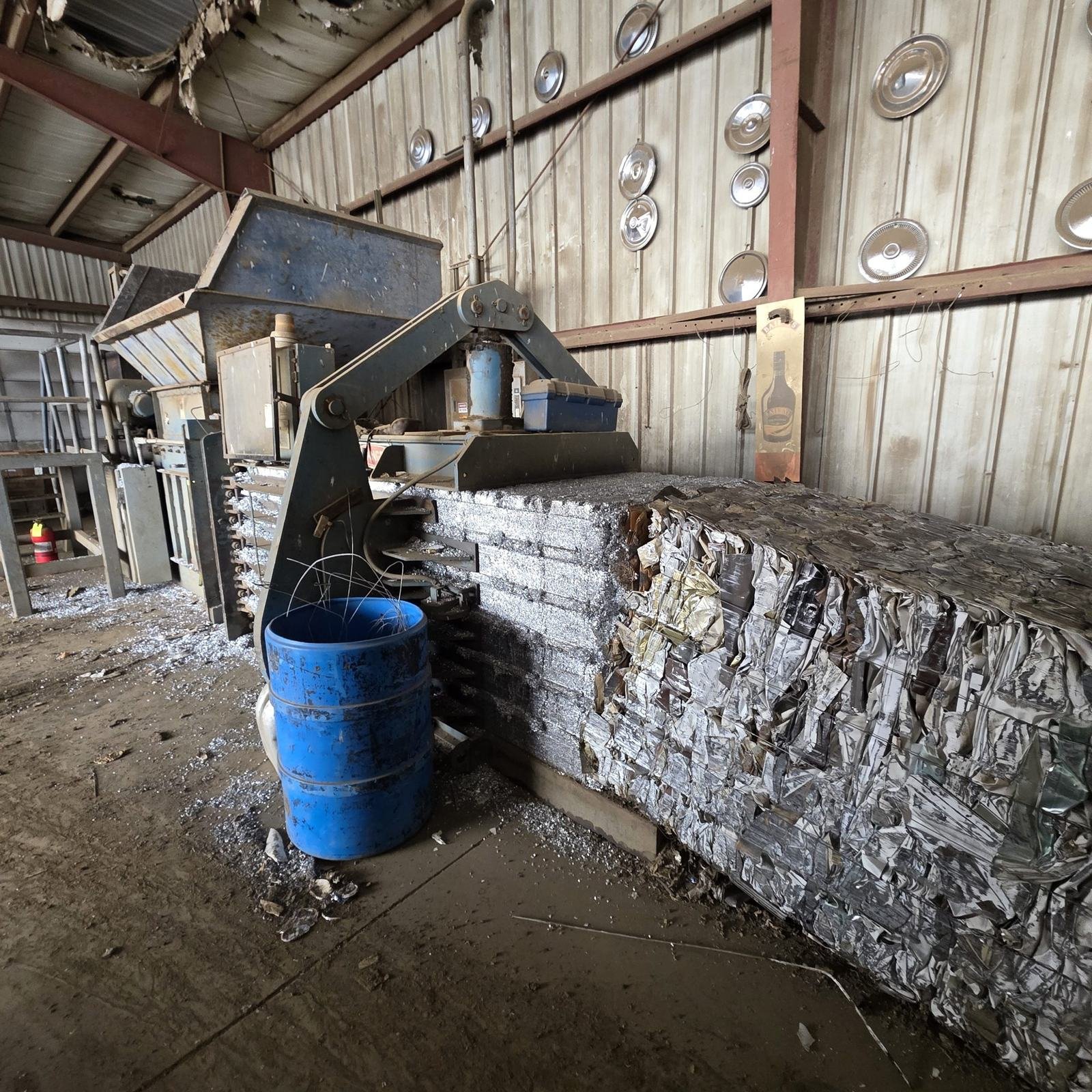 Bales of scrap metal stacked inside a recycling building beside the baler.