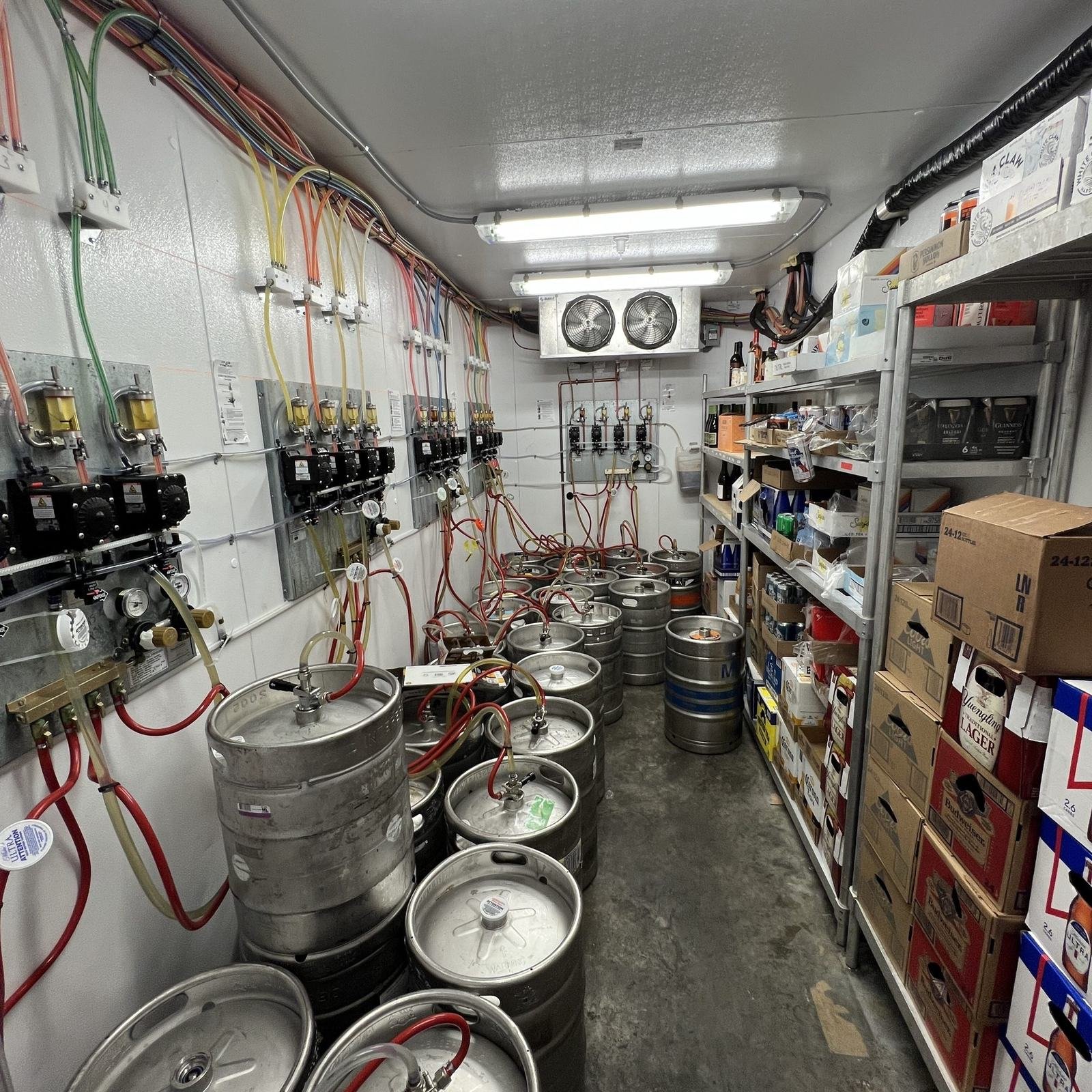 Inside a walk-in cooler holding beer kegs, draft lines and stock.