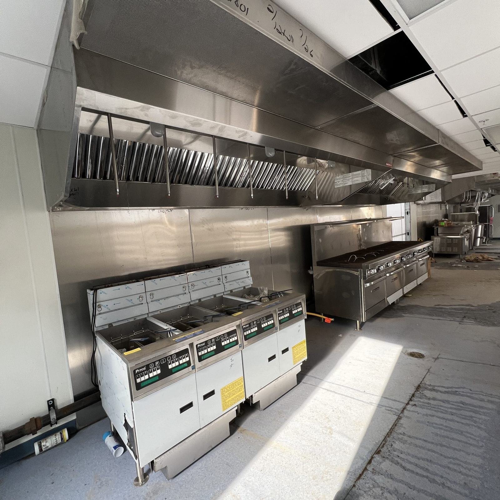 A stainless exhaust hood over a row of fryers and ranges on a restaurant cooking line.